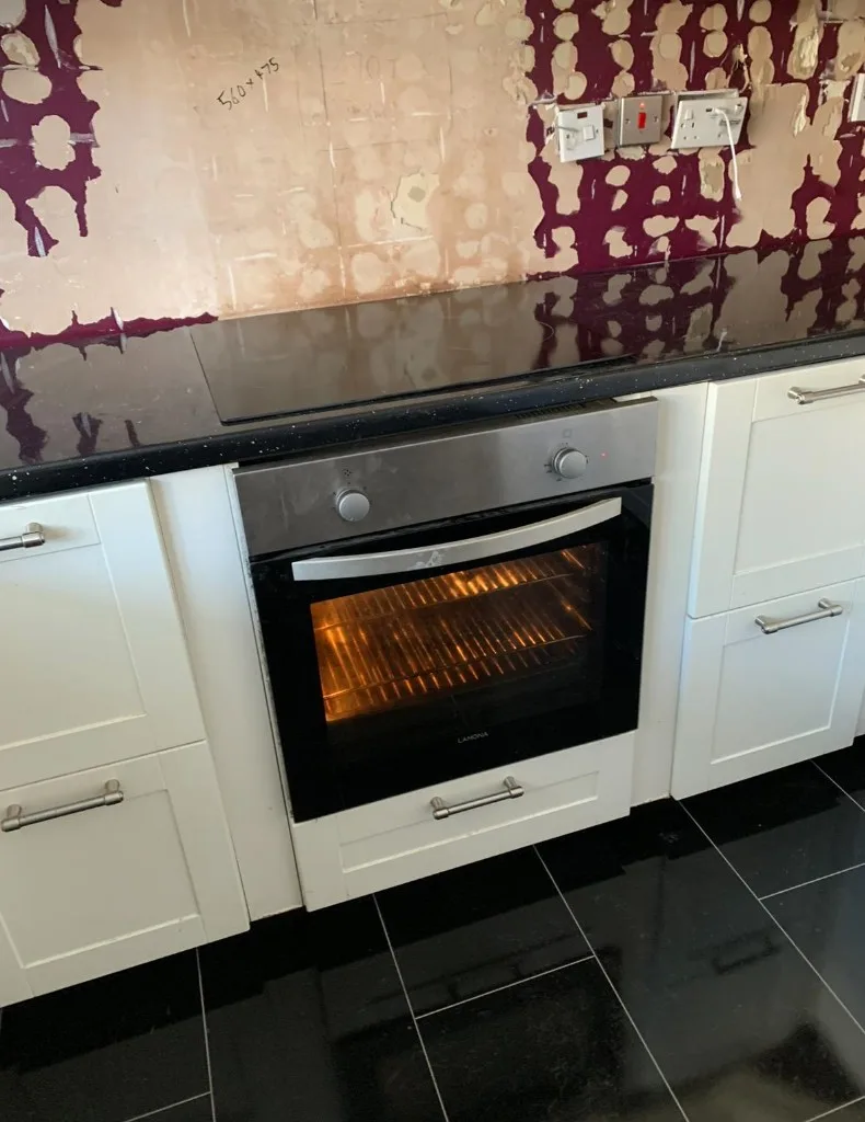 Black glass induction hob installed above Lamona oven with white shaker cabinets