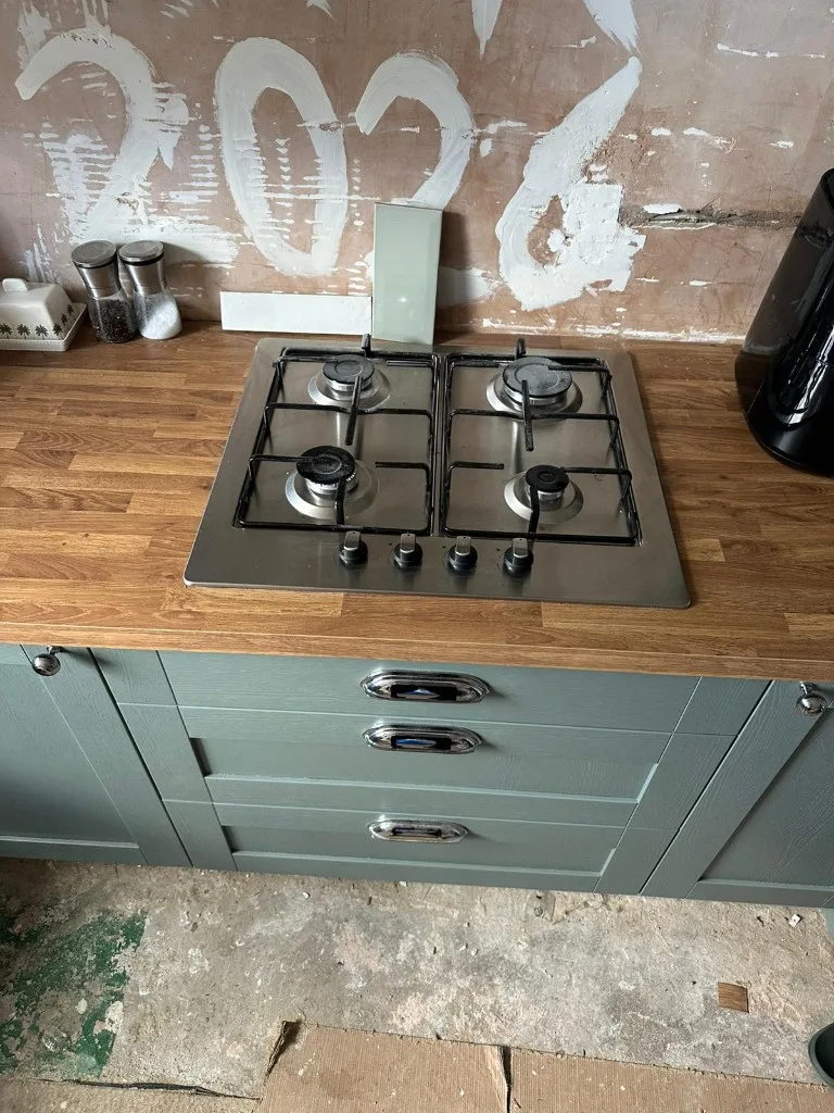 Stainless steel gas hob fitted into wooden worktop with sage green shaker drawers