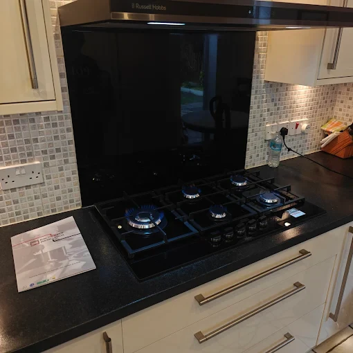 Five-burner gas hob with blue flames, black glass splashback and Russell Hobbs hood